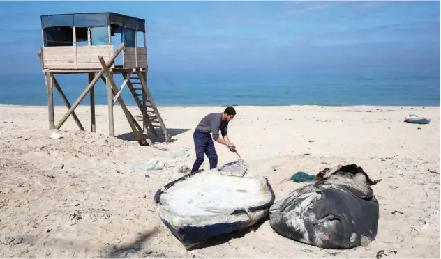  ?? Agence France-presse ?? A Palestinia­n fisherman moves a boat along the sandy beach in Khan Yunis in the southern Gaza Strip.