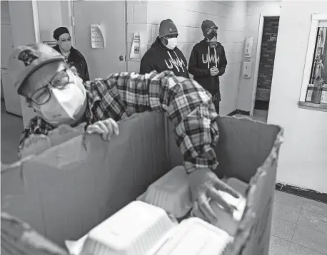  ??  ?? United Wholesale Mortgage concierge Quinton Chatman, background center, and Building Support Specialist Jeremy Moore, right, stand by as the Baldwin Center Executive Director Liz Longley looks over the food purchased from Berkley Common on Feb. 11.