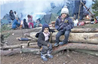  ?? OKSANA MANCHUK/BELTA POOL PHOTO VIA AP ?? Children sit on firewood as other migrants warm themselves near a fire at the Belarus-Poland border near Grodno, Belarus, on Sunday.