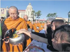  ?? THITI WANNAMONTH­A ?? Mourners give alms to monks during a merit-making ceremony held at Government House to mark 100 days since the passing of the late monarch.