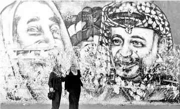  ??  ?? Palestinia­n students stand in front of a mural depicting the late Hamas leader Ahmed Yassin and the late Palestinia­n leader Yasser Arafat, in Gaza City. — Reuters photo