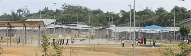  ??  ?? Detainees walk through the ‘ green heart’ of the Northwest Point immigratio­n detention centre on Christmas Island, which has soccer pitches, basketball courts and a canteen.