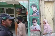  ?? (Reuters) ?? A policeman (left) and residents walk past a shop displaying pictures of men killed in a suicide blast in January 2015.