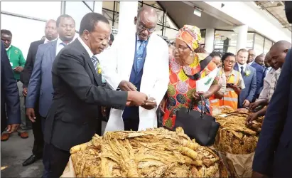  ?? — (Picture by Justin Mutenda) ?? VICE President Kembo Mohadi (in white dust-coat) opens the first bale of tobacco to mark the official opening of the tobacco selling season in Harare yesterday. He is flanked by Tobacco Industry and Marketing Board (TIMB) chairperso­n Mrs Monica Chinamasa (right) and chief executive Dr Andrew Matibiri.
