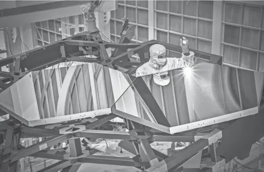  ?? CHRIS GUNN/NASA/AP FILE ?? Engineer Larkin Carey examines two test mirror segments on a prototype at the Goddard Space Flight Center’s giant clean room in Greenbelt, Md., in 2014. The James Webb Space Telescope will attempt to look back in time 13.7 billion years, a mere 100 million years after original stars from the Big Bang were forming.