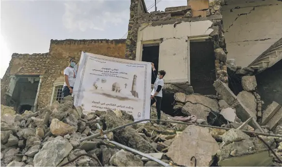  ?? AFP ?? Young people unfurl a poster welcoming Pope Francis to Iraq, next to the ruins of Al Tahera church in Mosul. The UAE is funding the reconstruc­tion of the building