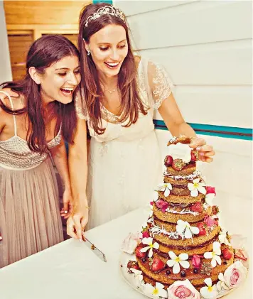  ??  ?? Ella Mills, who runs food blog Deliciousl­y Ella, takes a piece from her wedding cake alongside fellow blogger Olivia Wollenberg