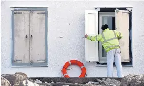  ??  ?? A man takes precaution­s at a property on the Cumbrian coast yesterday