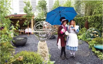  ??  ?? A file photo taken on May 18, 2015, shows exhibitors dressed as “The Hatter” (L) and “Alice in Wonderland” drinking tea whilst sheltering from the rain under an umbrella on the David Harbor stand at the 2015 Chelsea Flower Show in London. — AP