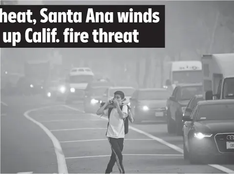  ?? ROBYN BECK, AFP/GETTY IMAGES ?? A man leaving Santiago Canyon College in Orange, Calif., protects himself Oct. 9 as Santa Ana winds blow fire and smoke toward the college. Another Santa Ana wind event is forecast for Monday and Tuesday.