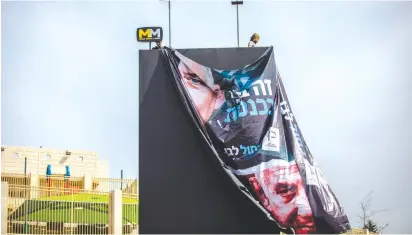  ?? (Yonatan Sindel/Flash90) ?? WORKERS HANG a large election campaign poster in Jerusalem last week.