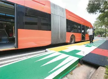  ?? STEPHEN M. DOWELL/ORLANDO SENTINEL ?? Passengers disembark a bus at a colorful elevated bus stop along Amelia Street in Creative Village on July 19. It’s an example of “quick build” infrastruc­ture plans, to put together temporary fixes to traffic and safety issues, bypassing the typical lengthy time periods for funding/designing more permanent solutions. This one on Amelia is expected to last six months, and has the chance to be permanent.