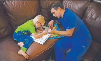  ??  ?? Spencer Cushing, a 29-year-old nurse who works in St. Jude Medical Center’s covid-19 unit, helps his 3-year-old son, James, color animation characters in Orange, Calif., after working a 12-hour shift at the hospital. For the month of April, the Cushing family lived apart. Cushing spent his days and some of his nights at St. Jude’s, as a nurse caring for “stepdown” patients recovering from the most serious covid-19 symptoms.