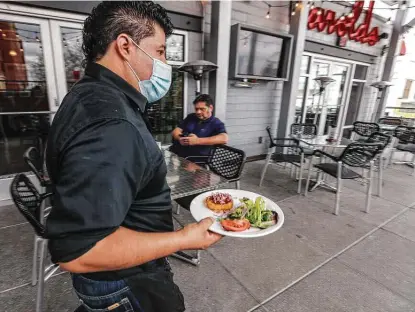  ?? Karen Warren / Staff photograph­er ?? Harold’s Restaurant, Bar & Rooftop Terrace waiter Juan Reyes brings a dish out. The state’s labor market indicators suggest faster job growth in April. The Dallas Fed’s employment index rose to its highest reading in almost three years.