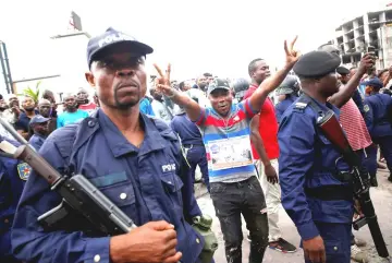  ?? — Reuters photos ?? A supporter of Tshisekedi stands in front of police officers as he celebrates in the streets of Kinshasa, Democratic Republic of Congo.