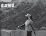  ?? Los Angeles Times/tns ?? A hiker wearing a mask because of the coronaviru­s walks past the Hollywood sign in Griffith Park on Monday.