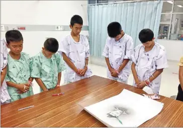  ?? HANDOUT / MINISTRY OF HEALTH / CHIANG RAI PRACHANUKR­OH HOSPITAL / AFP ?? Members of the ‘Wild Boars’ football team bow after writing messages on a drawing of a Navy SEAL diver who died during the rescue mission.