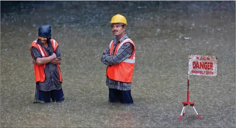  ?? REUTERS ?? Civic workers stand next to a sign at a flooded road due to heavy rains in Mumbai on friday.