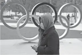  ?? TOMOHIRO OHSUMI/GETTY IMAGES ?? A woman wearing a face mask walks past the Olympic rings in front of the new National Stadium in Tokyo.