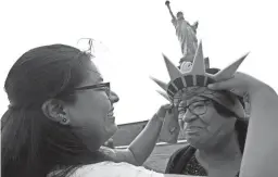  ??  ?? Karen Mejia fits her mother, Leonor Chipayo, with a souvenir visor while visiting the Statue of Liberty on Wednesday in New York City.