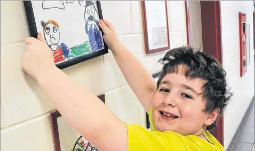  ?? MILLICENT MCKAY/JOURNAL PIONEER ?? Liam Trainor hangs his drawing on Athena Consolidat­ed School’s art gallery wall. The school started displaying students’ artwork as a way to build confidence and self esteem, while providing an outlet to student who may not be involved in other...