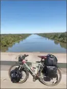  ??  ?? Ryan Wilcox snaps a photo of his bike by the Tombigbee River in Alabama, a quick pit stop in his cycling journey across the U.S.