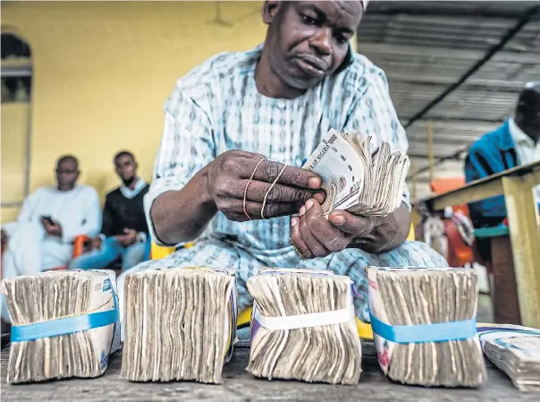  ?? /Bloomberg ?? Footdraggi­ng: currency dealer uses a mobile phone as he counts Nigerian naira banknotes for exchange on the black market in Lagos, Nigeria. Banks are said to be reluctant to take to the fintech era.