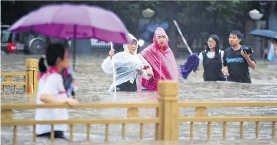 ?? (Photo: AP) ?? People walk through floodwater­s along a street in Zhengzhou in central China’s Henan Province, on Tuesday.