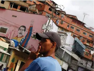  ?? (Carlos Barria/Reuters) ?? A CARACAS resident waits for a bus last week, with graffiti of Venezuela President Nicolas Maduro in the backdrop.