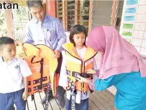  ??  ?? FATIMAH
memakaikan jaket keselamata­n kepada murid yang menaiki perahu semasa ke sekolah sambil dibantu oleh cikgu Nasrah Titing.