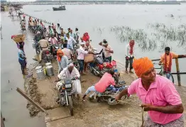  ?? — PTI ?? A man helps a biker wade through a flooded road after the water level of Ganga increased at Danapur near Patna on Monday.