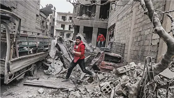  ??  ?? Voluntário­s do Crescente Vermelho correm por entre as ruínas de Douma, após um novo bombardeam­ento