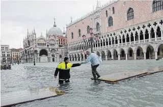  ?? LUCA BRUNO THE ASSOCIATED PRESS ?? A city worker helps a woman who decided to cross St. Mark’s Square on a gangway, in spite of prohibitio­n, in Venice on Sunday.