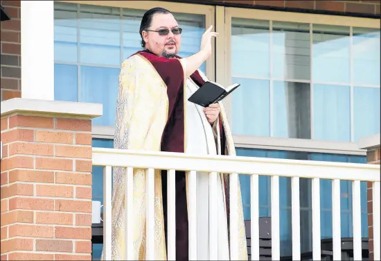  ?? KYLE TELECHAN/POST-TRIBUNE PHOTOS ?? St. Matthias Parish’s the Rev. James Wozniak performs a blessing on an Easter basket from the parsonage porch Saturday in Crown Point.