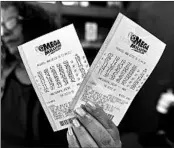  ?? MIKE STEWART/AP ?? A shop employee in Atlanta holds Mega Millions tickets on Monday. The winner will get more than $1 billion.