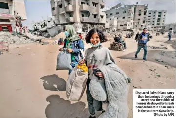  ?? ?? Displaced Palestinia­ns carry their belongings through a street near the rubble of houses destroyed by Israeli bombardmen­t in Khan Yunis in the southern Gaza Strip. (Photo by AFP)