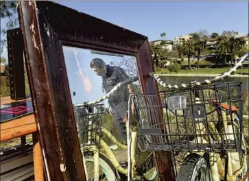  ?? Wally Skalij Los Angeles Times ?? LAPD OFFICER Adrian Gonzalez looks over belongings left behind at Echo Park by the homeless people who had camped there as the city began cleanup Friday. The park’s closure drew protests and relief from residents.