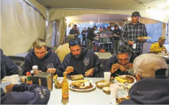  ??  ?? Firefighte­rs eat dinner at the Rana base camp. The Food Unit Leader estimated last week that the cook staff had prepared more than 400,000 meals for firefighte­rs and support staff.