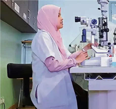  ??  ?? Universiti Malaya medical graduate Dr Lina Yusrina Iskandar Zulkarnain (left) uses a slit lamp to examine a patient’s eye in the ophthalmol­ogy clinic.