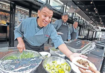  ?? MATT STONE / BOSTON HERALD ?? PAYING UP: Manuel Martinez, Junior Del Toro and Tomas Martinez of Tacos Tumbas a Tomas in Los Angeles make free tacos for Red Sox fans after L.A.’s Grand Central Market lost a bet with Faneuil Hall Marketplac­e when the Red Sox beat the Dodgers in the World Series. At top, Sox fans Will Hattery and Gary Short Jr., both of Reading, take a bite of their free tacos.