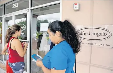  ?? AMY BETH BENNETT/STAFF PHOTOGRAPH­ER ?? Carolina Villegas, 33, ofWest Palm Beach, left, and Yadira Castro, 27, ofWest Palm Beach, stand outside Alfred Angelo Bridal in Boynton Beach emailing a law firm listed on a paper sign in the window.