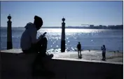  ?? ARMANDO FRANCA — THE ASSOCIATED PRESS ?? A young man checks his phone by the Tagus river at Lisbon's Comercio square on a sunny winter day on Jan. 30.