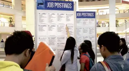  ??  ?? HOPEFULS line up looking at job listings in a job fair.