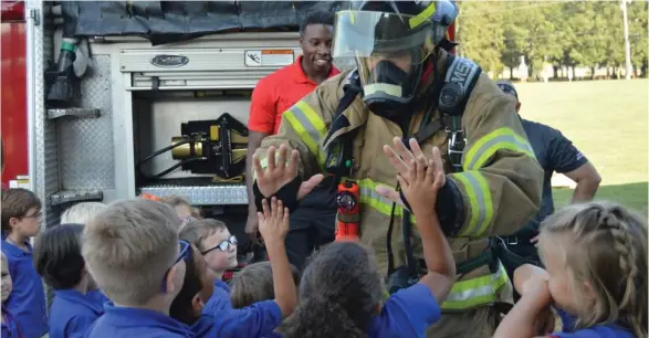  ?? Sarah Raines, SDN) (Photo by ?? SFD firefighte­r Josh Cox gives high fives to children in Starkville Academy teacher Jamie Hunt's kindergart­en class during the Safety Town event on Tuesday.