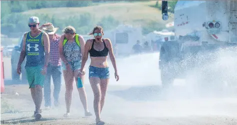  ?? MICHAEL BELL ?? Victoria Faith, centre, and her friends keep cool in the steamy temperatur­es with spray from a water truck at Country Thunder in Craven.