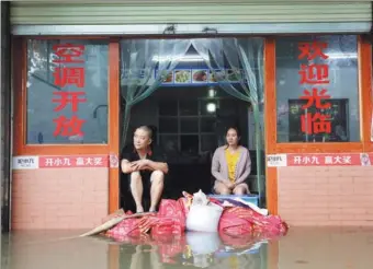  ?? LIU CHANGSONG / FOR CHINA DAILY ?? Owners of a small diner sit at the doorway as sandbags are used to hold off floodwater­s in Suining, Sichuan province, on Tuesday.