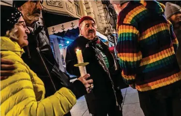  ?? Stephen Lam/The Chronicle ?? Richard Maggi (center) holds a candle Sunday night at a vigil outside Harvey Milk’s former camera shop.