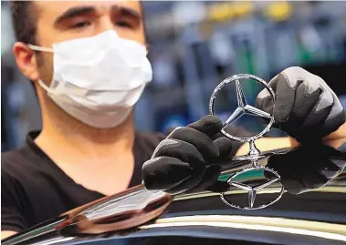  ?? MATTHIAS SCHRADER/ASSOCIATED PRESS ?? An employee wearing a face mask to protect against the spread of the new coronaviru­s attaches a Mercedes emblem to a Mercedes-Benz S-class car at the company’s plant in Sindelfing­en, Germany, in April.