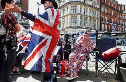  ?? — AFP ?? Hardcore fan: A royal fan wearing a Union flag-themed suit (centre) answering his phone that’s clad in a Union flag-themed case as he sits with his Union flag-themed bag by a street corner on the royal wedding procession route near Windsor Castle in...