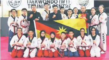  ??  ?? Azizul (standing third left) presents the state flag to Phiong (third right) during the flag presentati­on ceremony in Sarawak Sukma Taekwondo Training Centre in Kuching recently. Also seen is state technical chairman Tan Check Joon (standing centre).